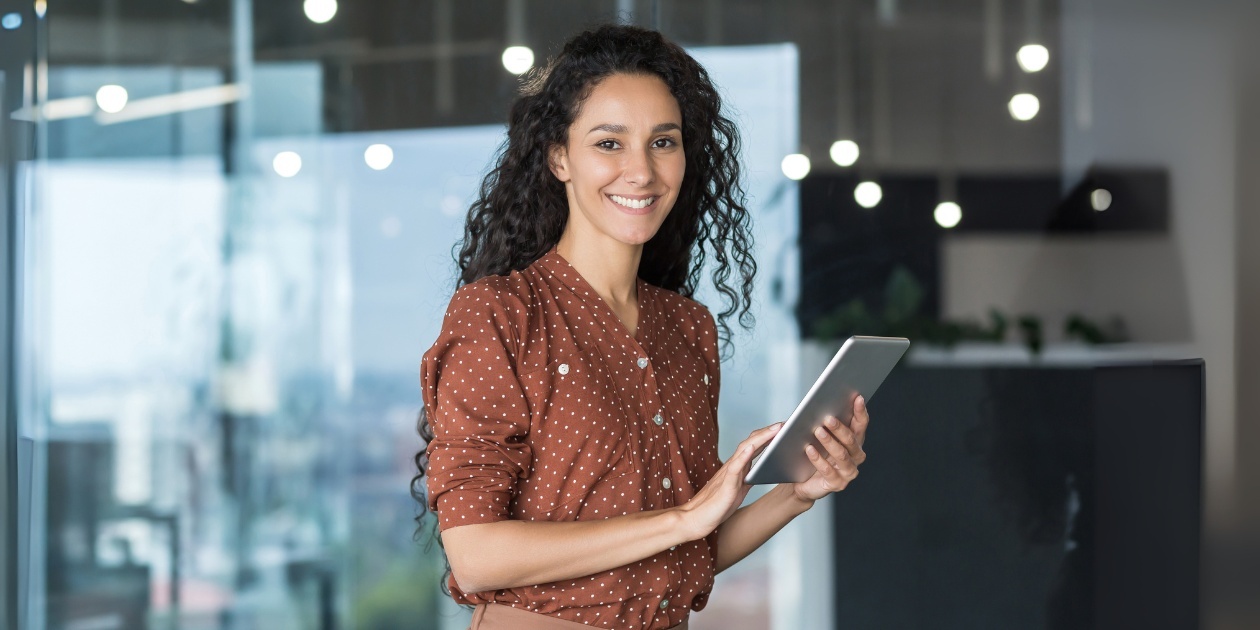 Woman in polka-dot shirt holding tablet in modern office, 50 characters