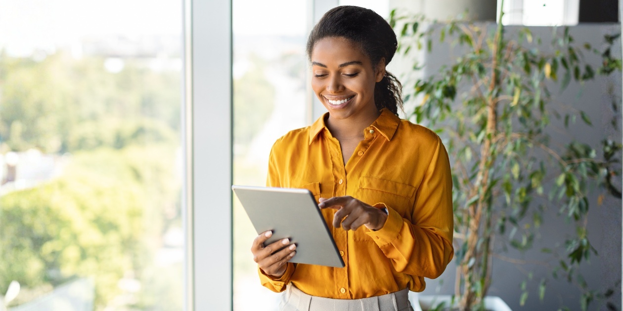 Smiling Professional Woman in Yellow Blouse Using Tablet in Modern Office