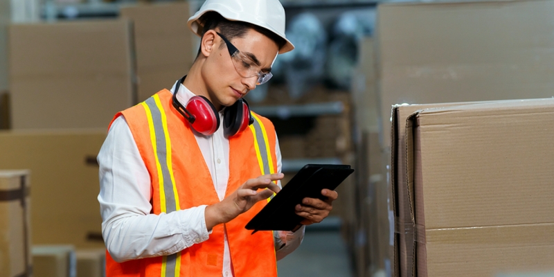 Worker with a hardhat and safety vest using a tablet.